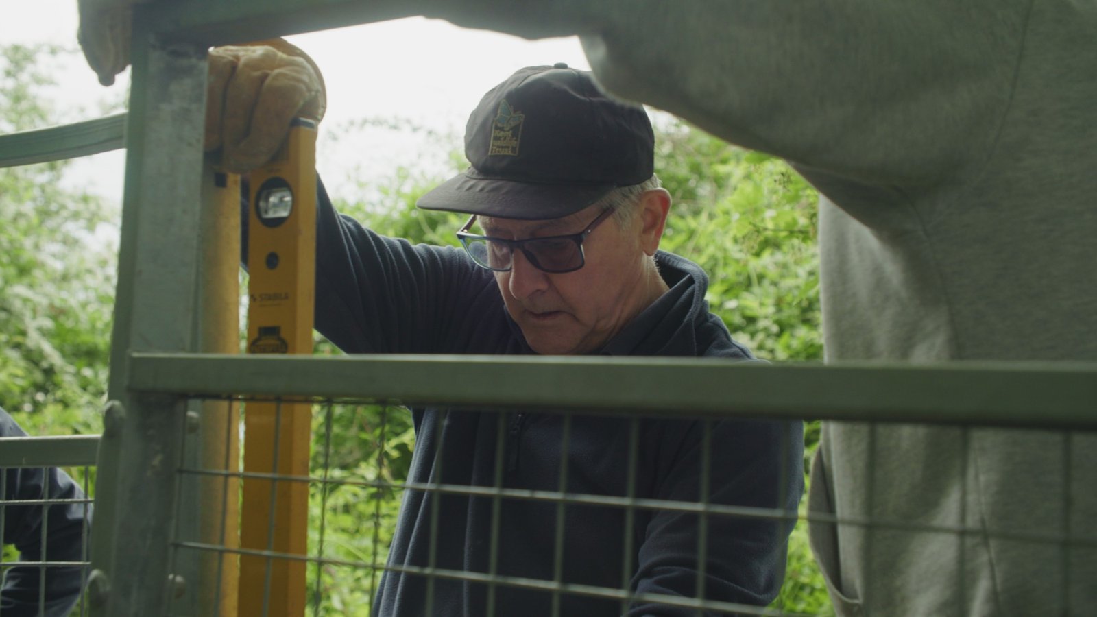 An older man using a spirit level while fixing a metal field gate