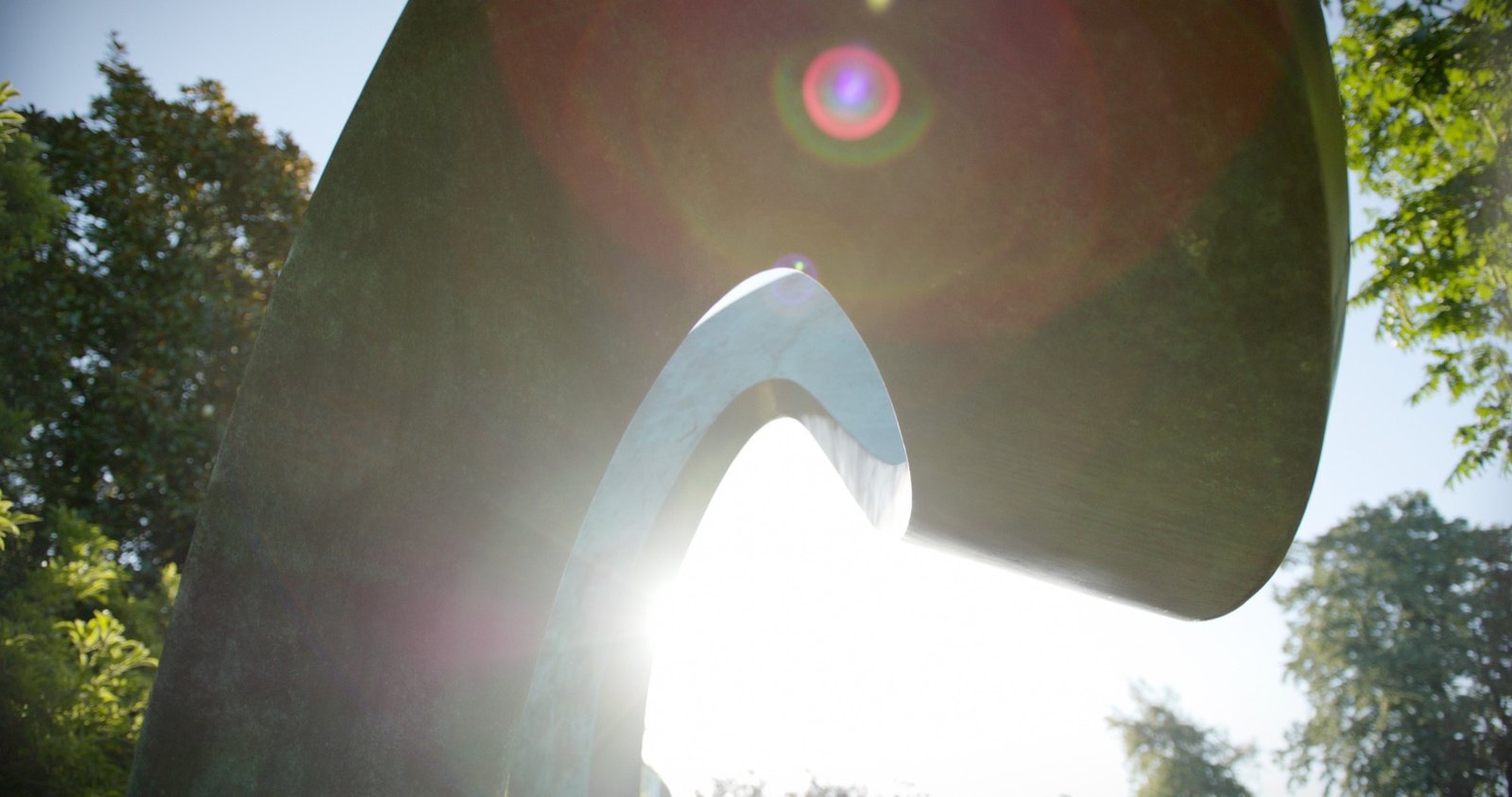 Sunlight flaring through the curves of an abstract metal sculpture in a garden