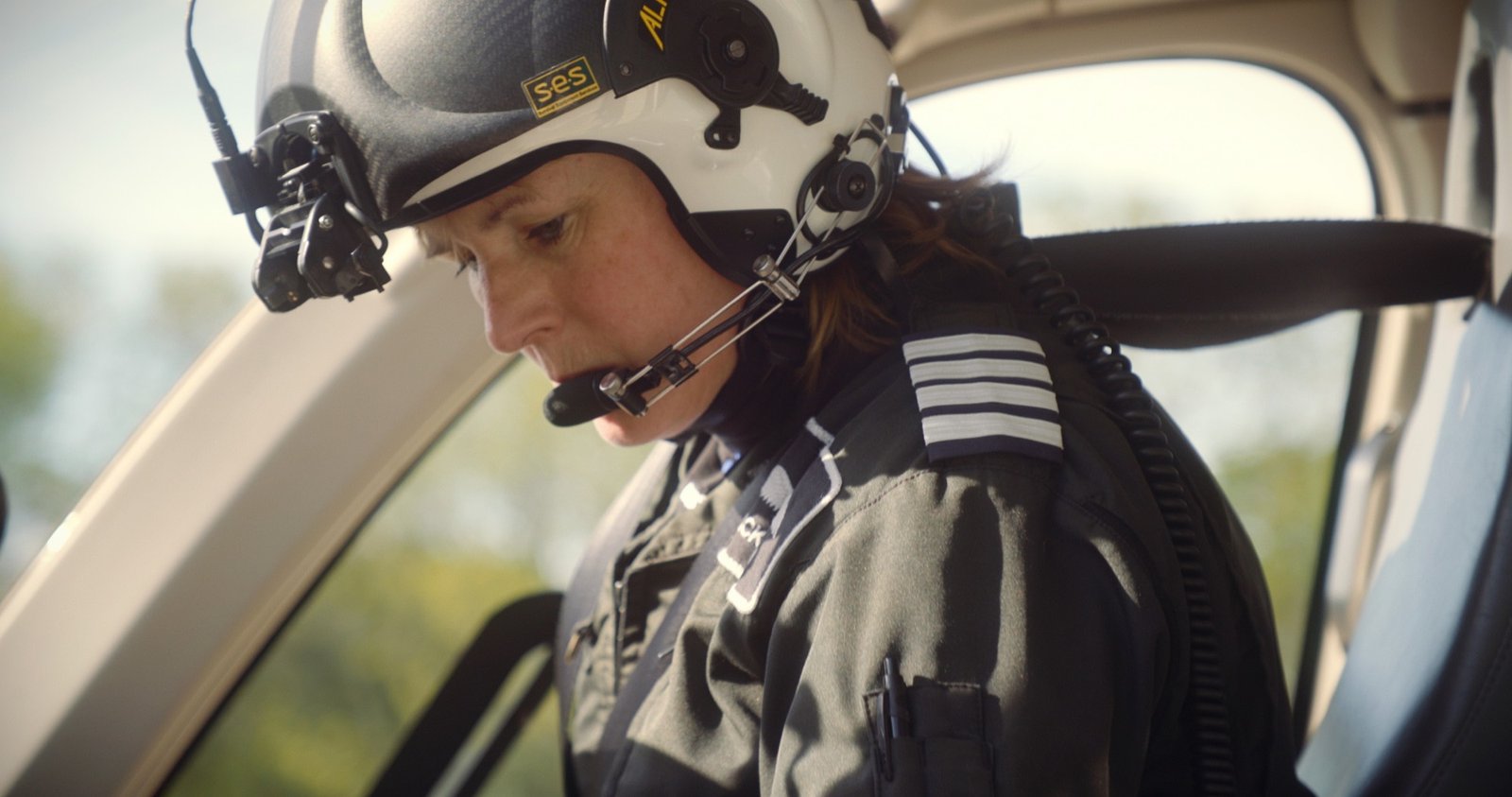 A woman in a flight helmet and headset seated in a helicopter cockpit